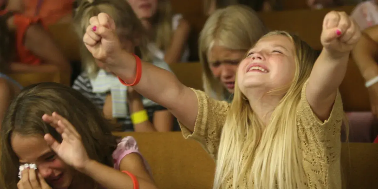 Junge Mädchen erleben emotionale Momente bei einer evangelistischen Religionsveranstaltung, eine jubelt, die andere weint.