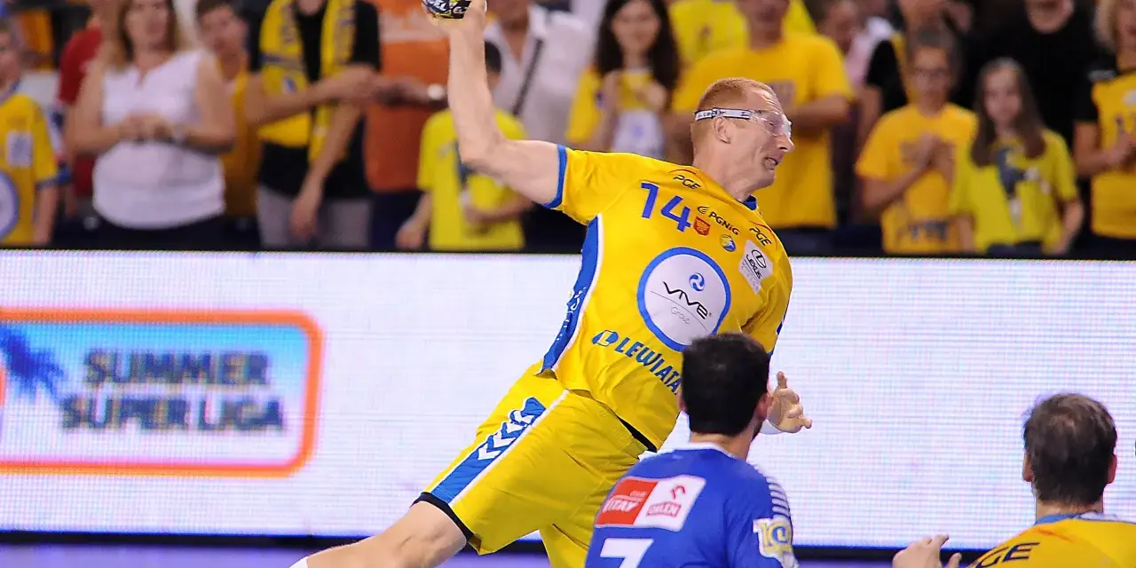 Piłkarz ręczny w żółtej koszulce z numerem 14 rzuca piłkę podczas eliminacji mistrzostw europy w piłce ręcznej grupa polska.