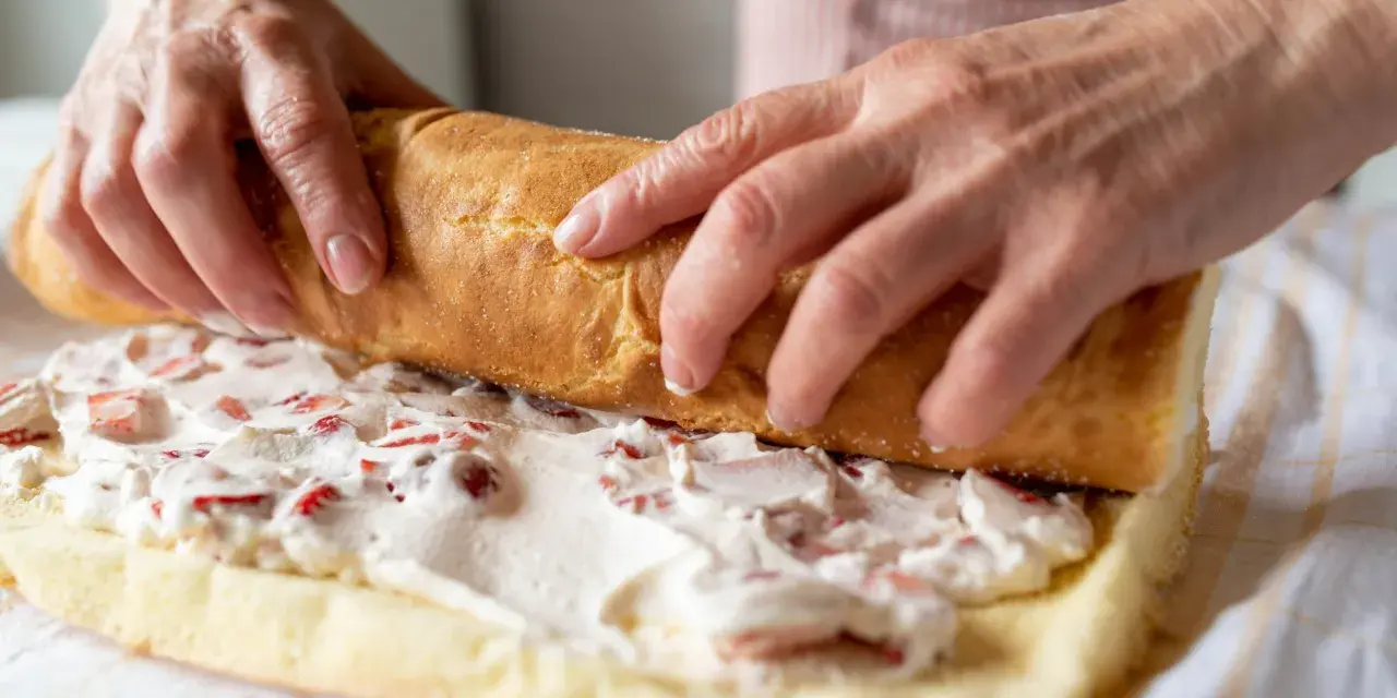 Ręce zwijają biszkopt z kremem i truskawkami. To najprostsza rolada biszkoptowa, która zachwyci smakiem.