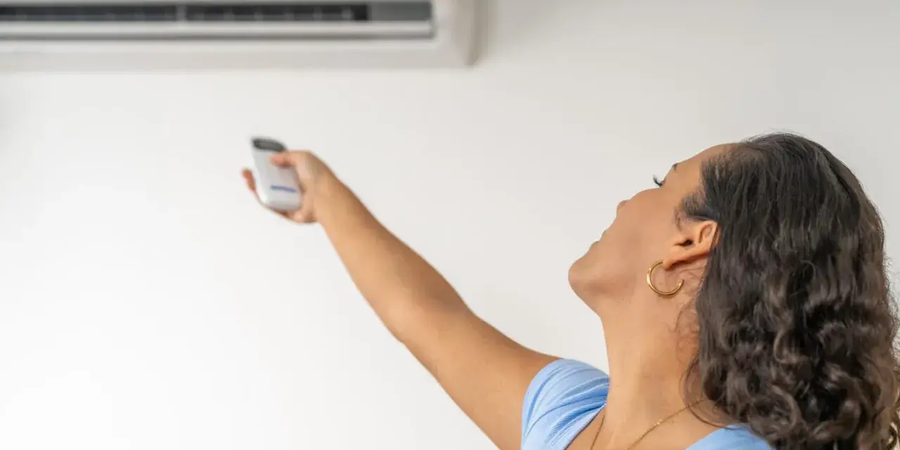 Donna con telecomando regola il condizionatore, la canalina condizionatore design si integra perfettamente.