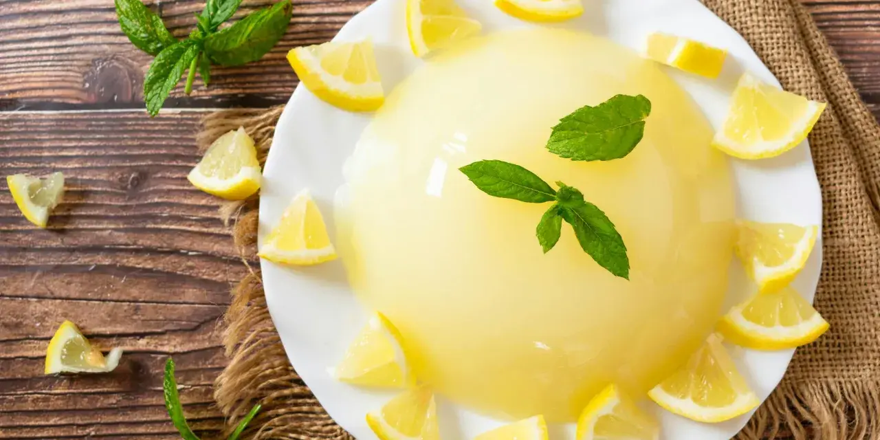 Delizioso gelo di limone su piatto bianco, decorato con spicchi di limone fresco e foglie di menta.