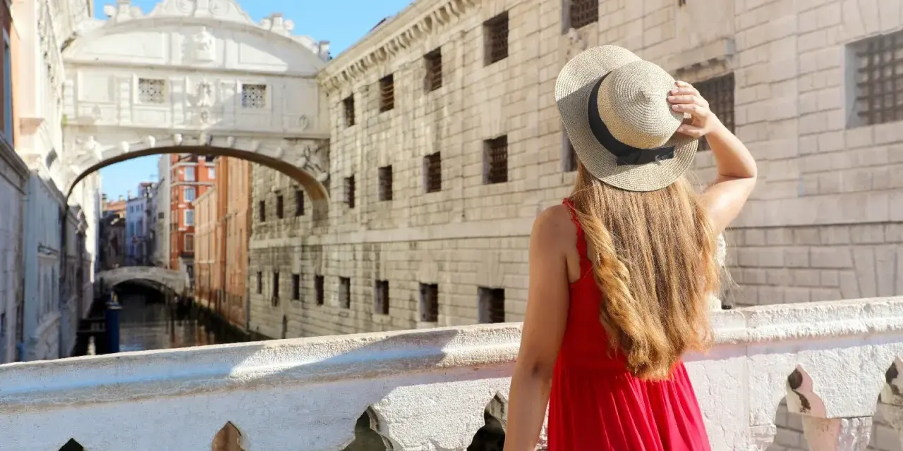 Una donna con un cappello di paglia ammira il Ponte dei Sospiri, un iconico ponte degli innamorati a Venezia, con i suoi canali e palazzi storici.