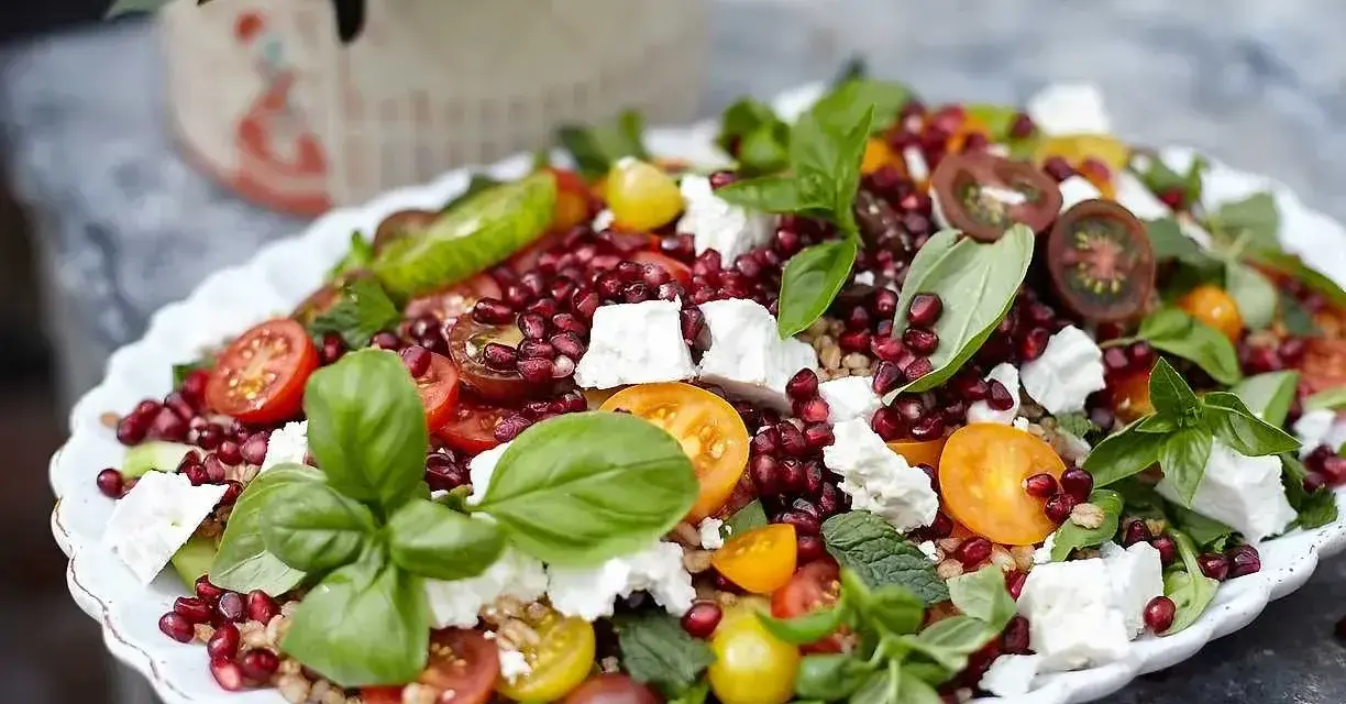 En färgglad sallad med granatäpple, tomater, fetaost och basilika, perfekt som sallad till grillat.
