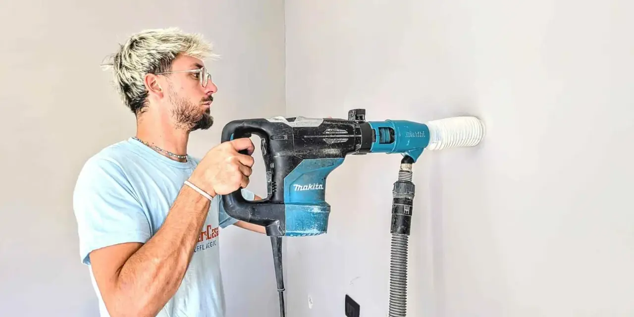 Giovane con capelli biondi usa un trapano Makita per fare un foro nel muro. Il trapano non buca muro, ma aspira la polvere.