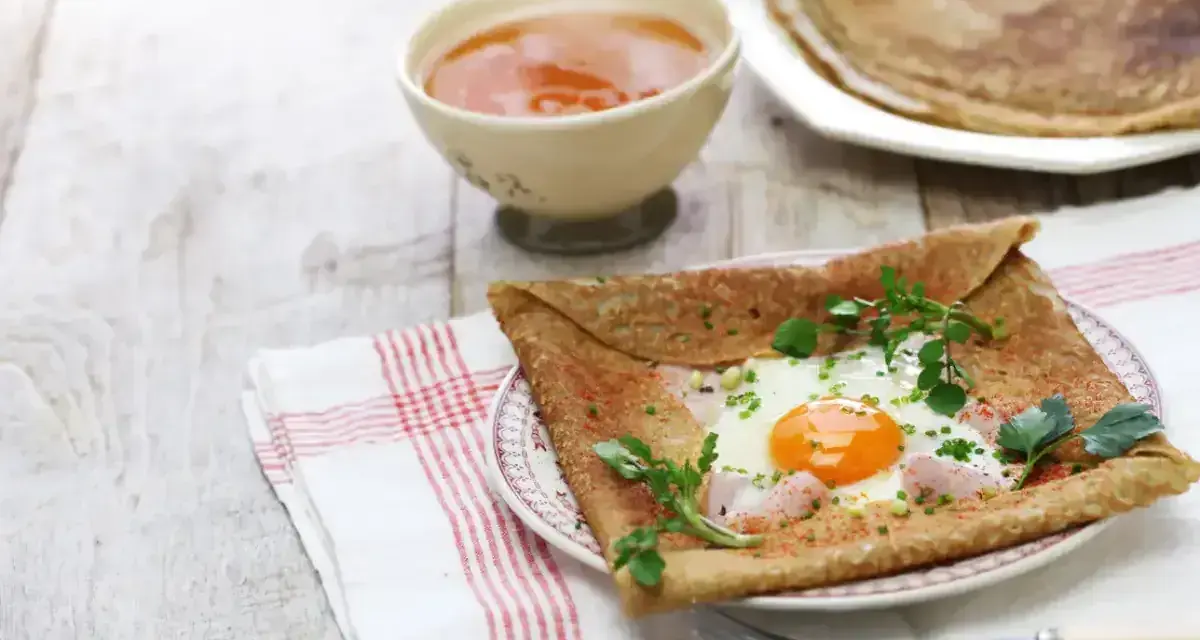 Crêpe de sarrasin garnie d'un œuf au plat, de jambon et d'herbes fraîches, servie avec une compote.