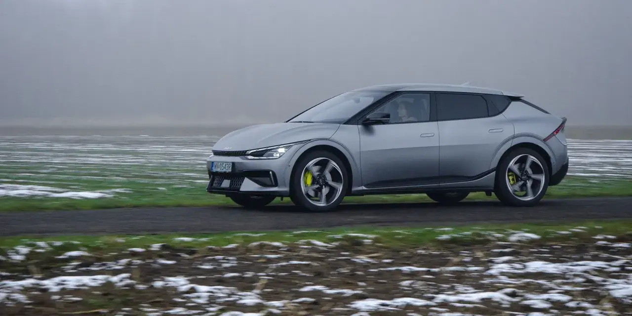 Srebrna Kia EV6 jedzie po drodze, otoczona polami z resztkami śniegu.
