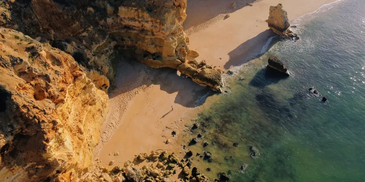 Malownicze klify i piaszczysta plaża w Portugalii. Morze o turkusowym odcieniu obmywa skaliste wybrzeże, tworząc idealne miejsce na spacer.