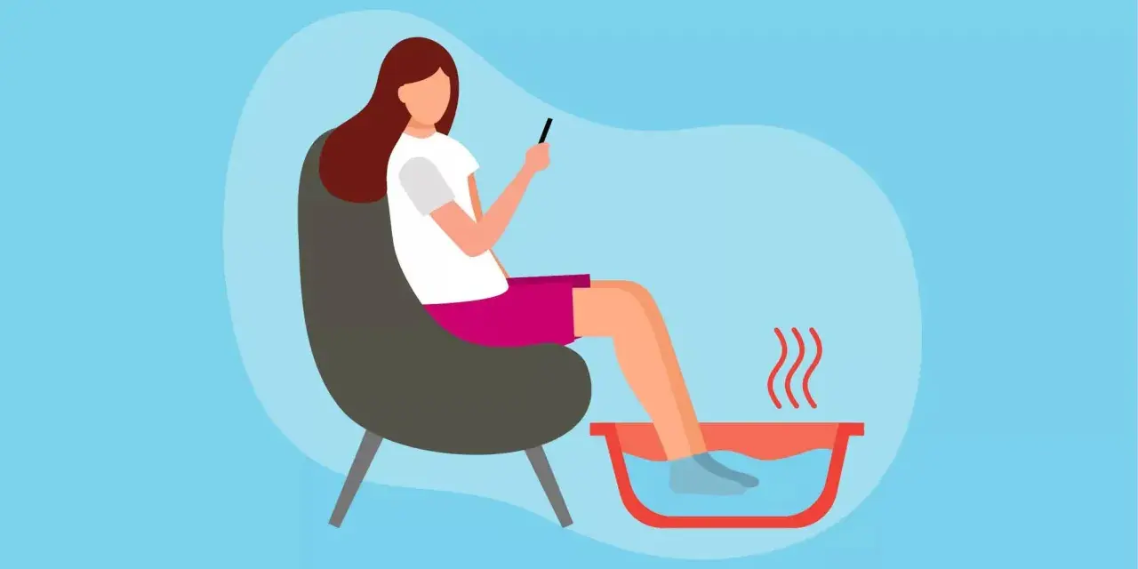 A woman relaxes in a chair, enjoying a soothing foot soak while scrolling on her phone.