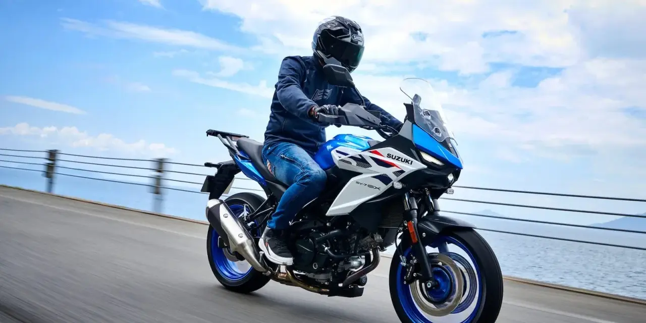 Motocyklista na niebiesko-białym Suzuki SV650X, idealnym motocyklu do 35kW, jedzie wzdłuż wybrzeża.