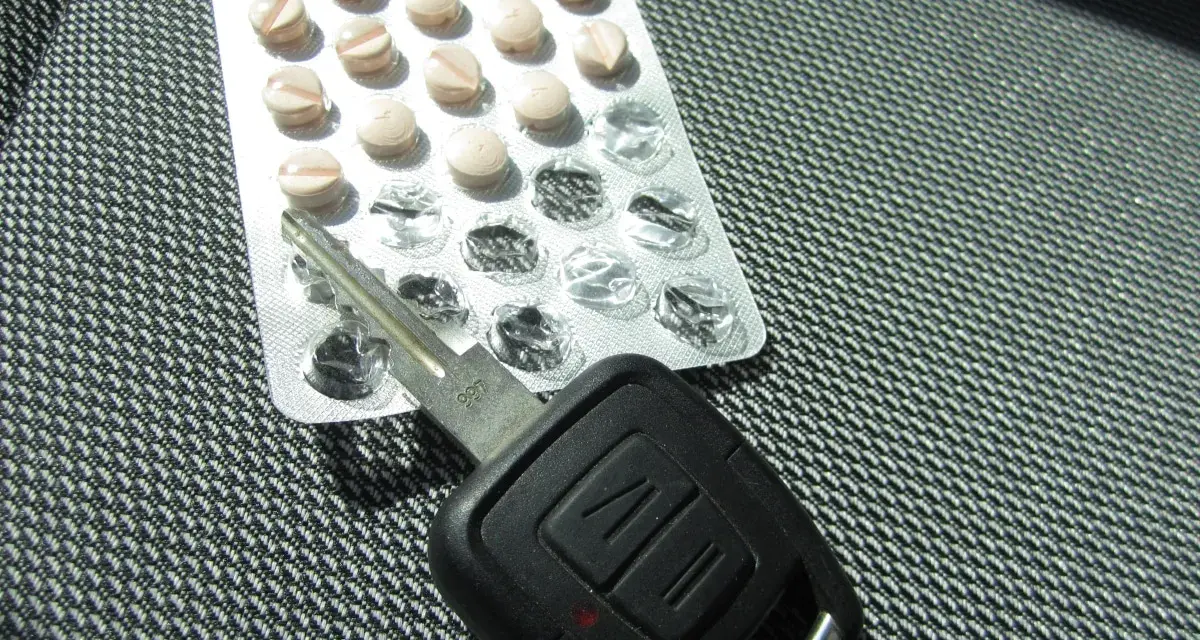 Tabletten und Autoschlüssel liegen nebeneinander. Tilidin autofahren ist gefährlich und illegal.