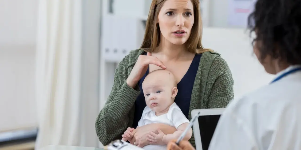Zaniepokojona mama z niemowlęciem na rękach rozmawia z lekarzem. Zastanawia się nad chwilowym zawieszaniem się dziecka.