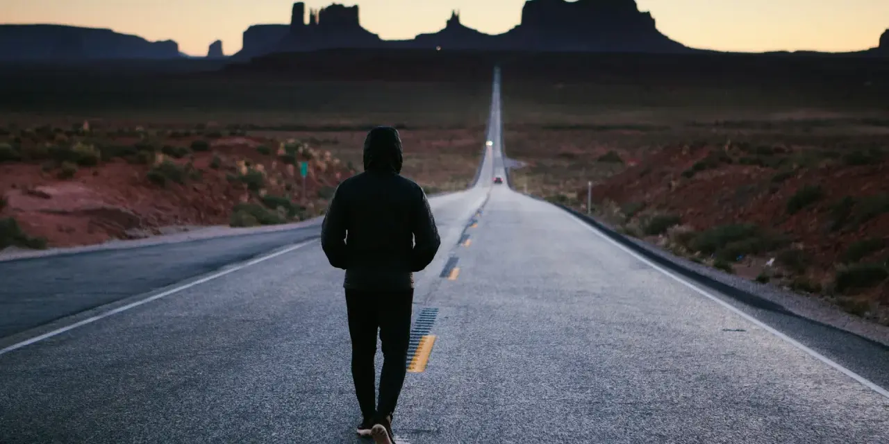 Człowiek idzie pustą drogą w Monument Valley, pogrążony w mysleniu tunelowym, z widokiem na skalne formacje w oddali.