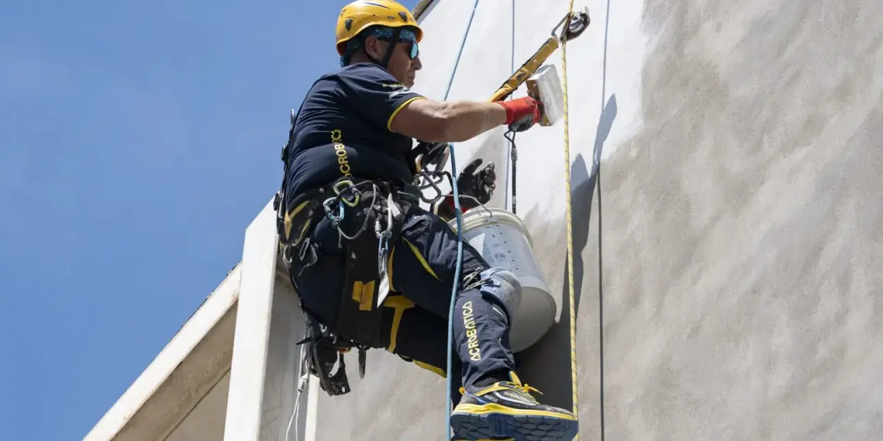 Trabajador en altura realiza instalación SATE, aplicando revestimiento en fachada con equipo de seguridad.