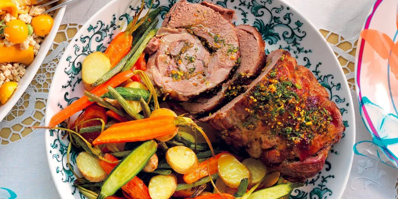 Agnello al forno succulento, affettato e servito con patate novelle, carote e fagiolini croccanti su un piatto decorato.