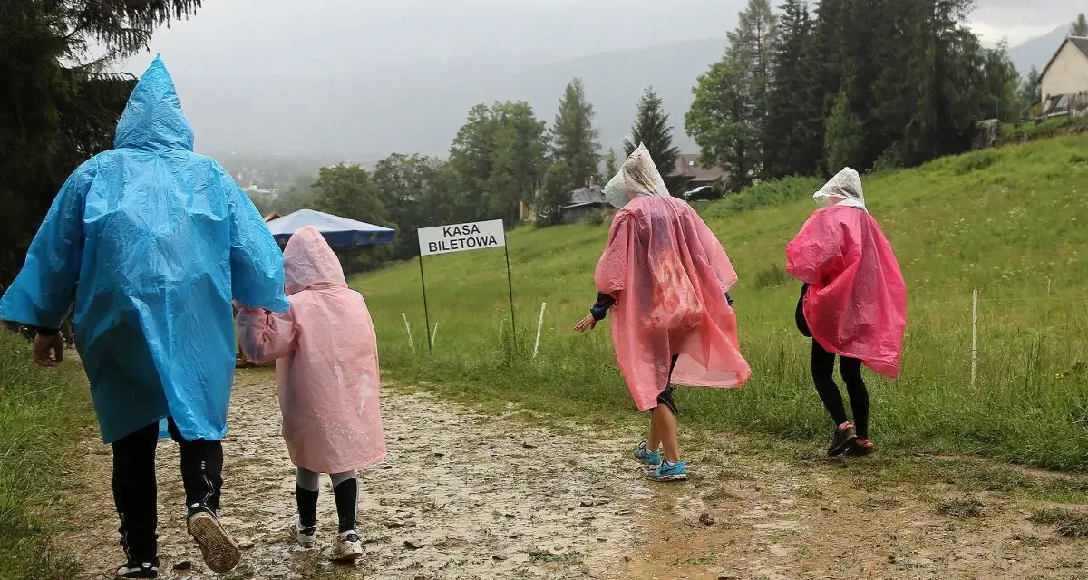 Deszcz w Zakopanem? Nic nie szkodzi! Rodzina w kolorowych pelerynach idzie ścieżką do kasy biletowej, ciesząc się widokami.