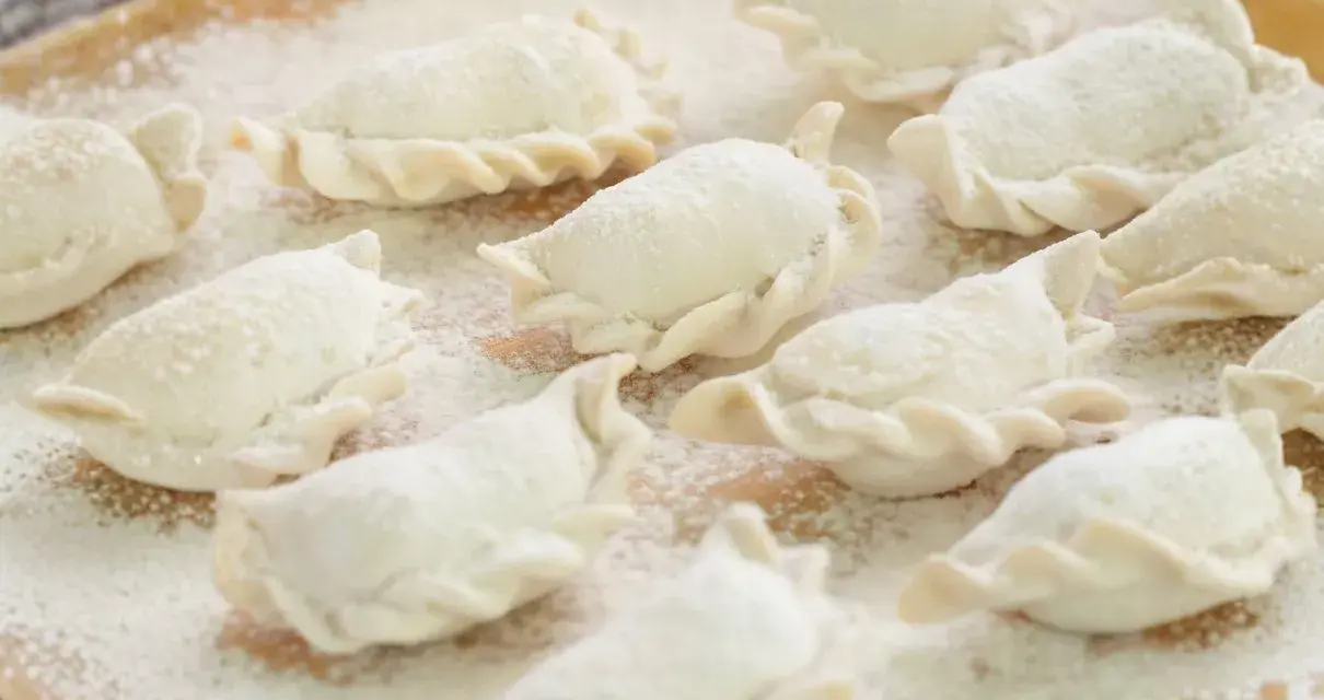 Surowe pierogi, gotowe do gotowania, posypane mąką. Wyglądają jak najlepsze ciasto na pierogi, które mama kiedyś robiła.