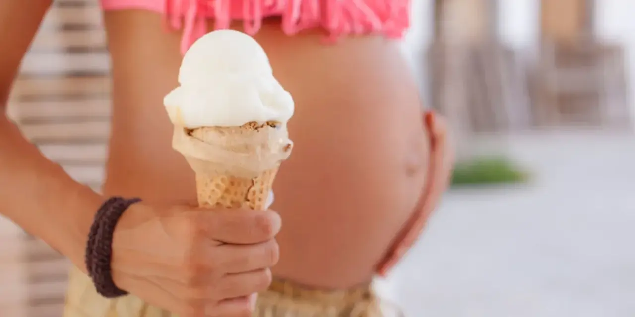Schwanger und Lust auf Eis? Eine Frau hält ein Eis in der Hand, während sie ihren Bauch streichelt.