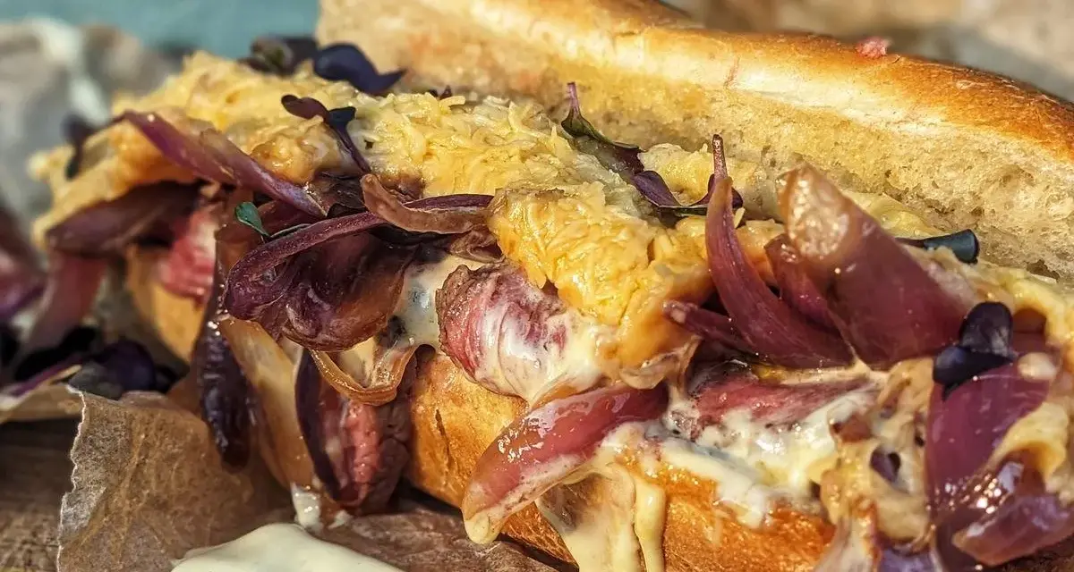 Ein saftiger Philly Cheesesteak-Sandwich mit geschmolzenem Käse, karamellisierten roten Zwiebeln und zartem Rindfleisch auf einem Baguette.