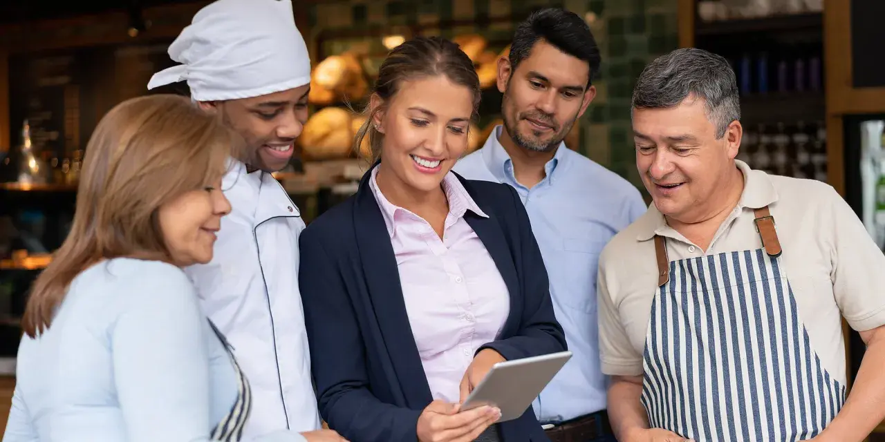Equipo revisando tablet para la gestión de restaurantes. Chef, gerentes y personal colaboran.