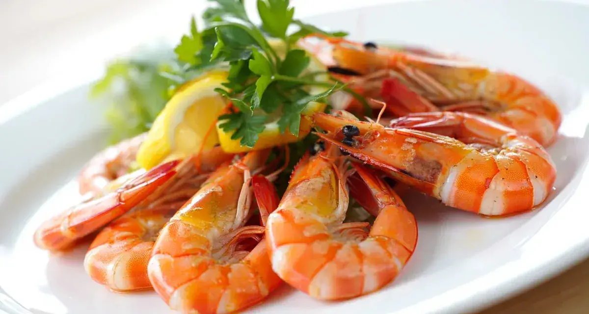 Gambas al ajillo receta: jugosas gambas cocinadas con ajo y perejil, servidas con limón y lechuga en un plato blanco.