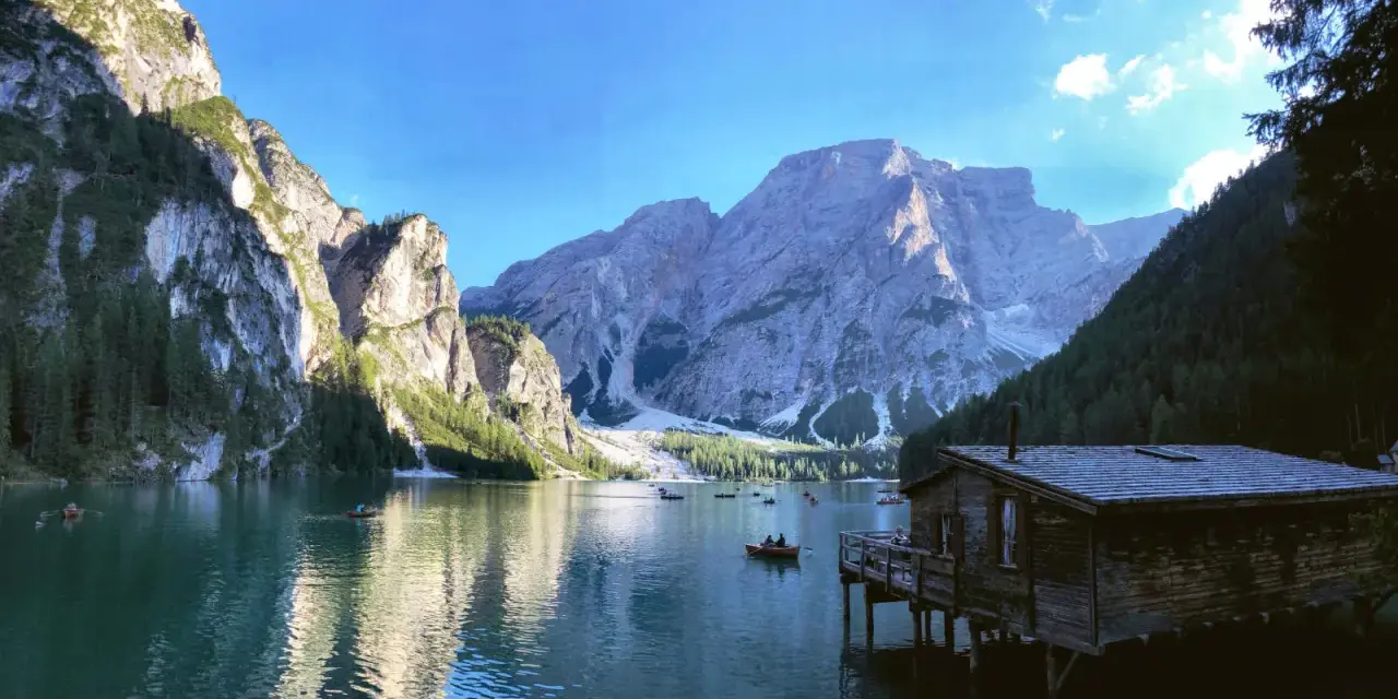 Malownicze jezioro w Dolomitach, z górami w tle i drewnianym domkiem na wodzie. Idealne miejsce na camping i podziwianie natury.