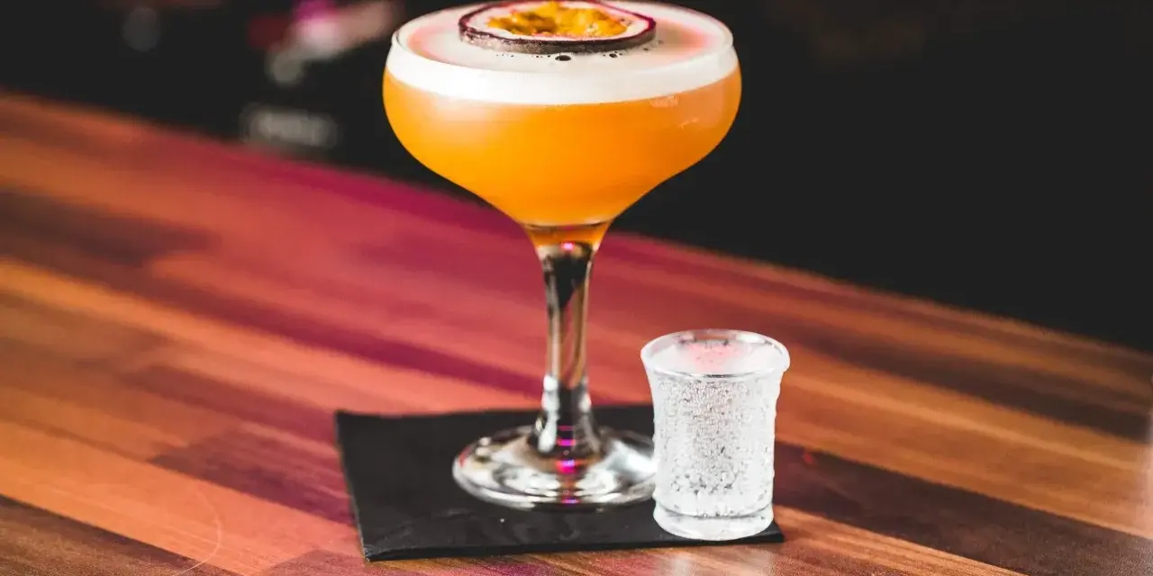 Orzeźwiający passion fruit martini z pianką i plasterkiem owocu, obok kieliszek wody gazowanej. Idealny na letnie wieczory.