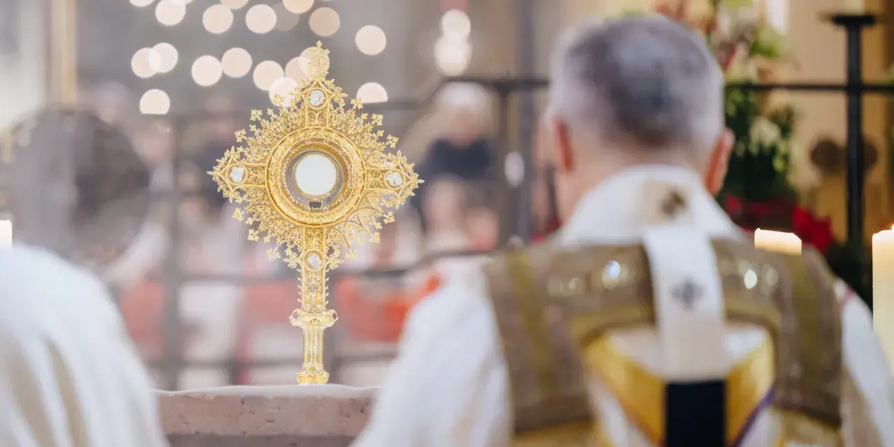 Goldene Monstranz mit Hostie im Schein von Kerzenlicht. Ein Priester in festlicher Kleidung feiert die Messe, ein Moment des weihnachtlichen Christentums.