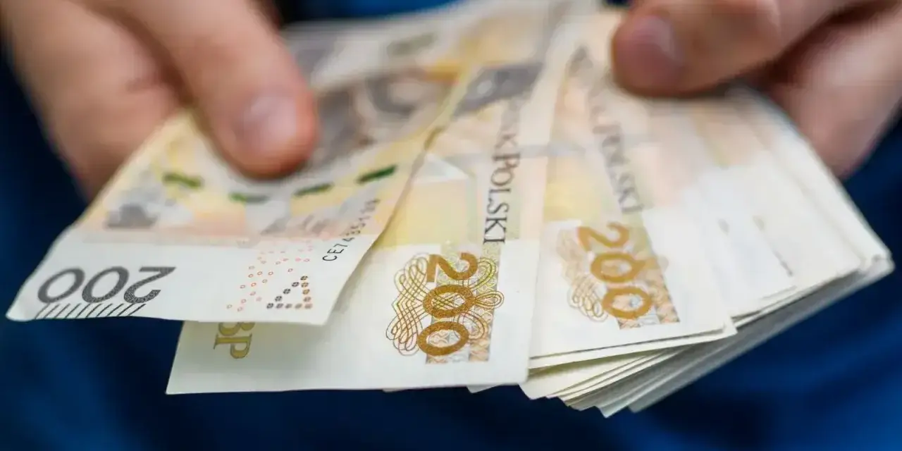 Dłonie trzymają stos banknotów 200 zł. Pieniądze mogą posłużyć do zapłaty czynszu administracyjnego.