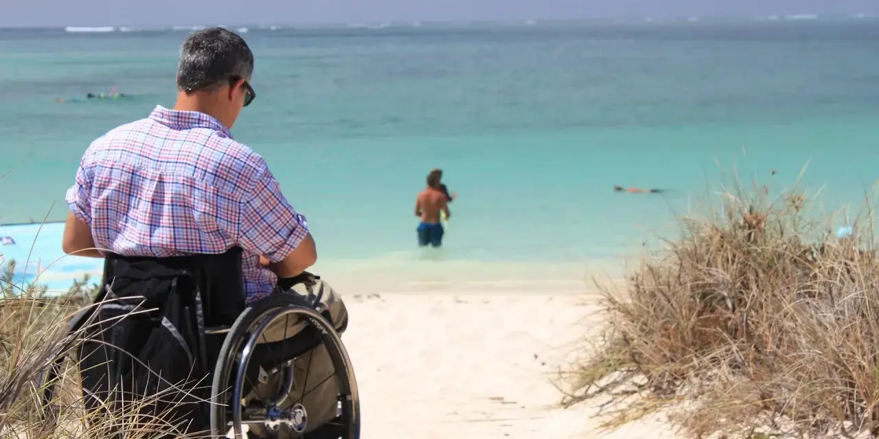 Mężczyzna na wózku inwalidzkim podziwia morze. Paraplegia co to? To utrata czucia i ruchu w nogach, ale nie ogranicza to radości życia.