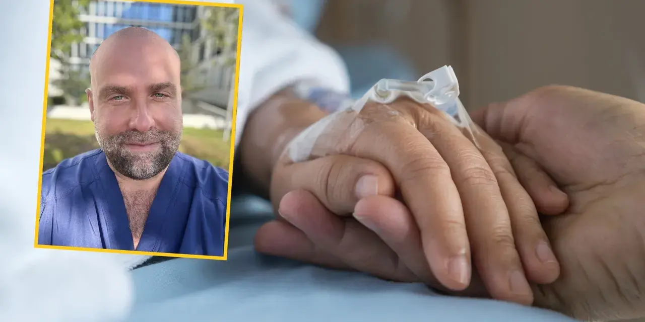 Uśmiechnięty mężczyzna w niebieskim uniformie medycznym podaje słowa otuchy choremu na raka, trzymając go za rękę z wenflonem.