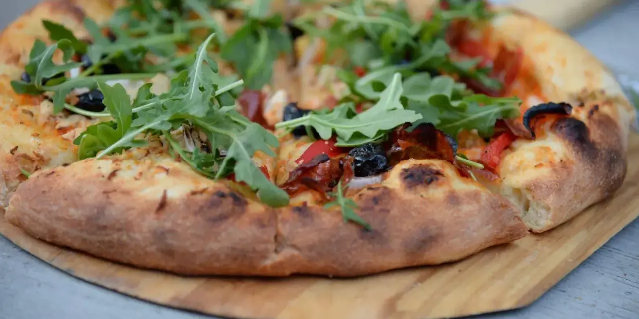 Idealne ciasto na pizzę z rukolą, oliwkami i papryką, wypieczone na drewnianej desce.