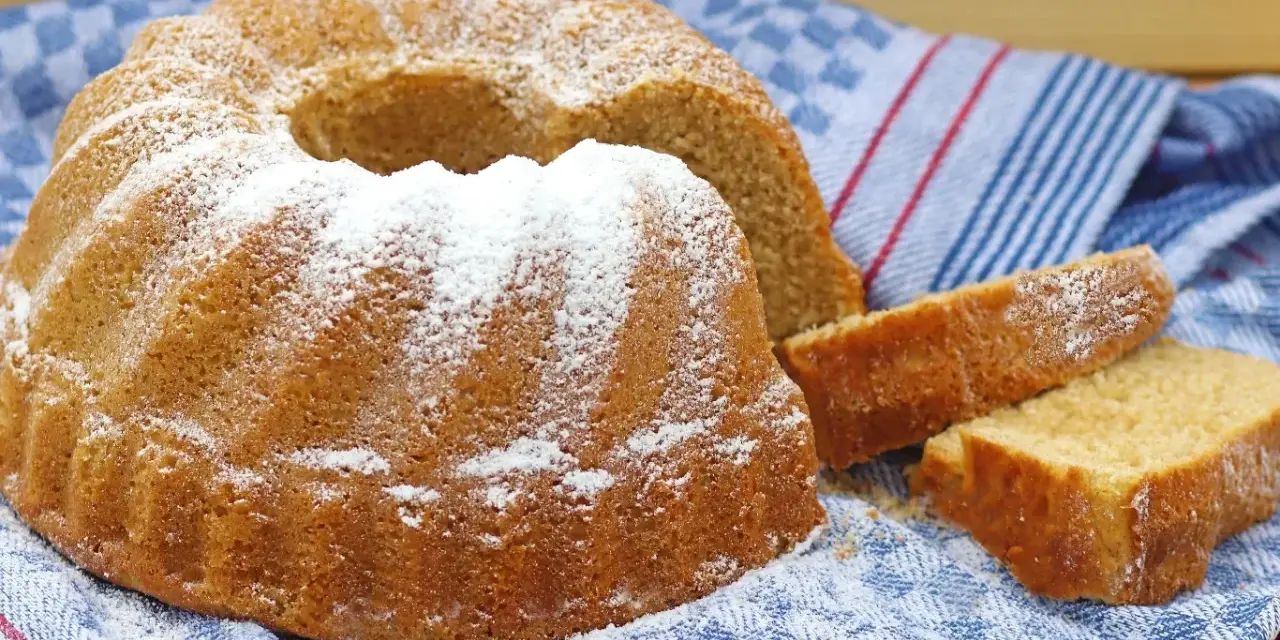 Puszysta babka z cukrem pudrem, obok niej kromki ciasta, na niebieskim ręczniku.
