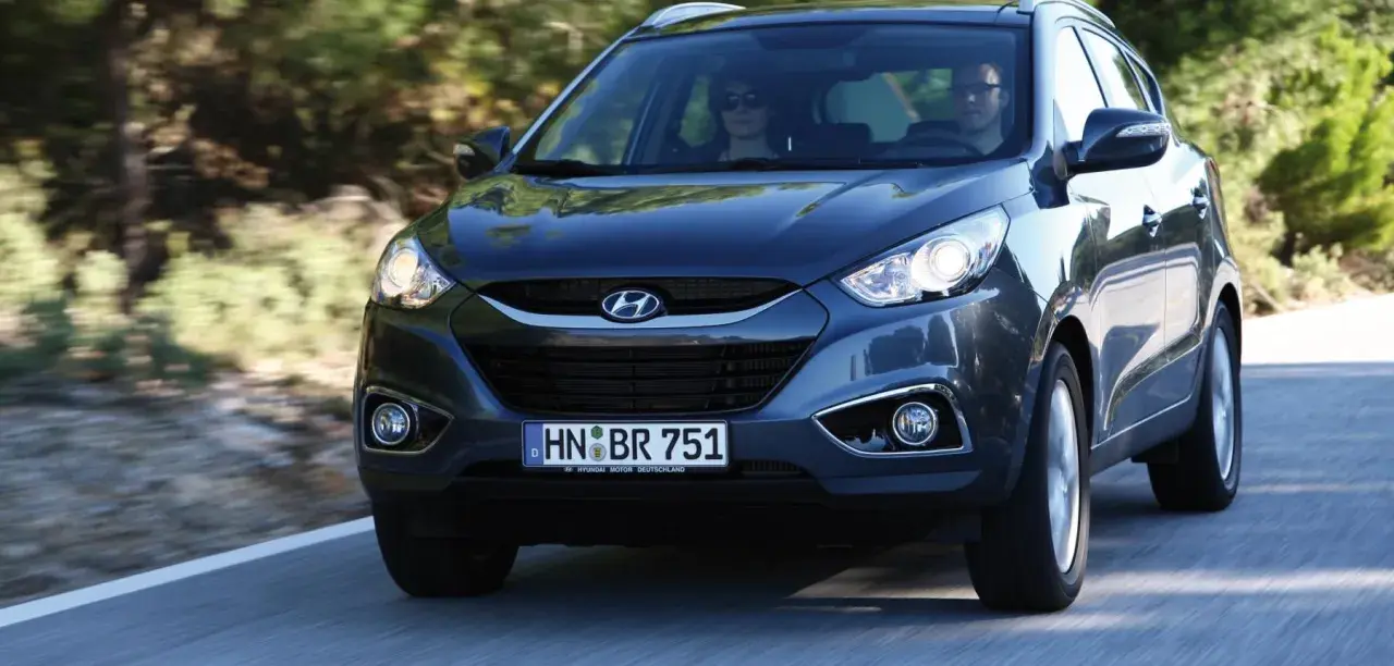 Dunkelgrauer Hyundai ix35 fährt auf einer Straße. Fahrer und Beifahrerin sind zu sehen. Mögliche Hyundai ix35 Probleme sind hier nicht ersichtlich.