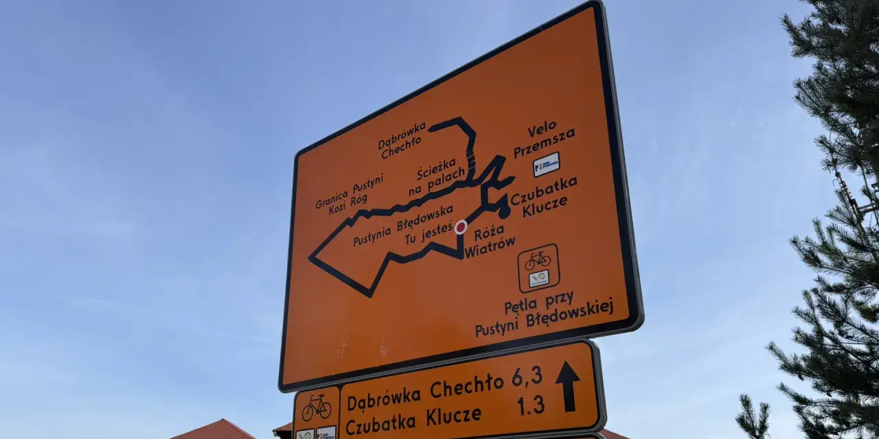 Pomarańczowa tablica z mapą szlaków rowerowych Velo Przemsza. Wskazuje drogę do Pustyni Błędowskiej, Czubatki Klucze i innych miejsc.