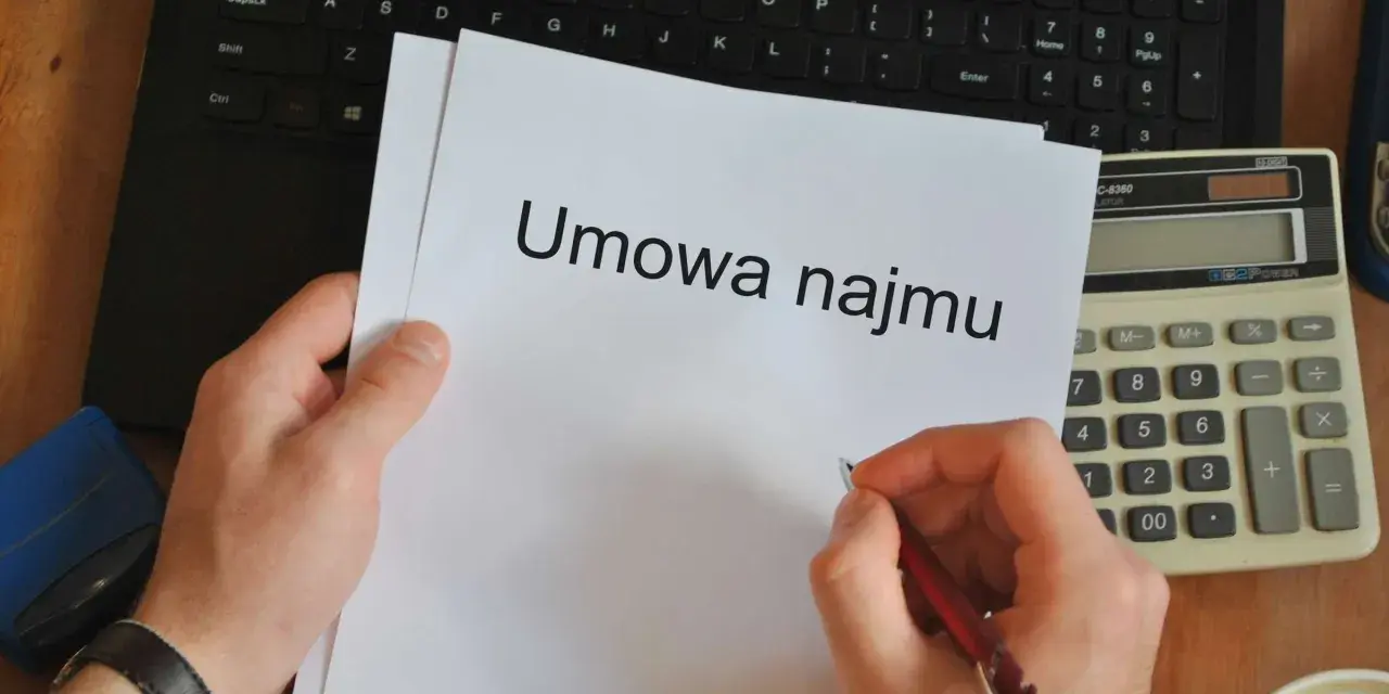 Ręka pisze długopisem na umowie najmu, obok kalkulator i laptop. Czas pomyśleć o podatku od najmu.