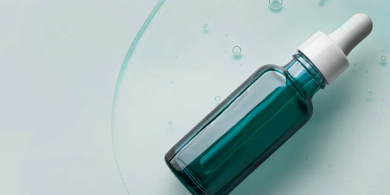 Szklana buteleczka z pipetką, wypełniona zielonym serum, na tle płynu z bąbelkami.