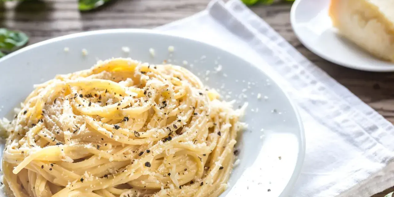 Szybki obiad z makaronem: spaghetti posypane parmezanem i pieprzem, obok kawałek sera i listki bazylii.