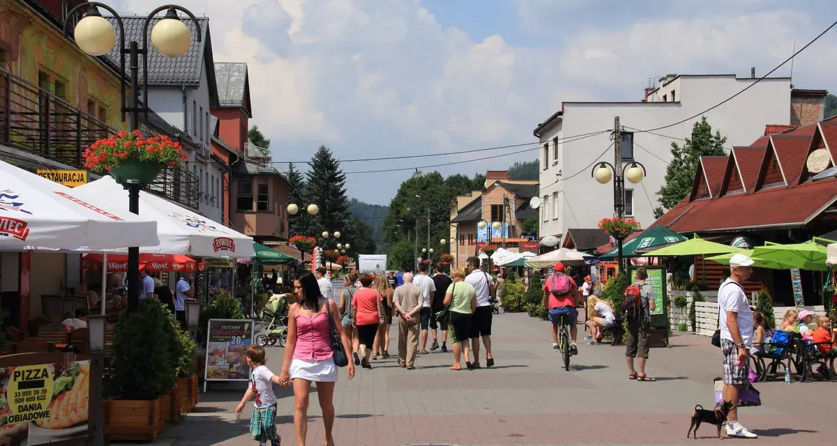 Tętniąca życiem ulica w Wiśle, pełna ludzi spacerujących, rowerzystów i psów. Wiele kawiarni i restauracji oferuje swoje atrakcje.