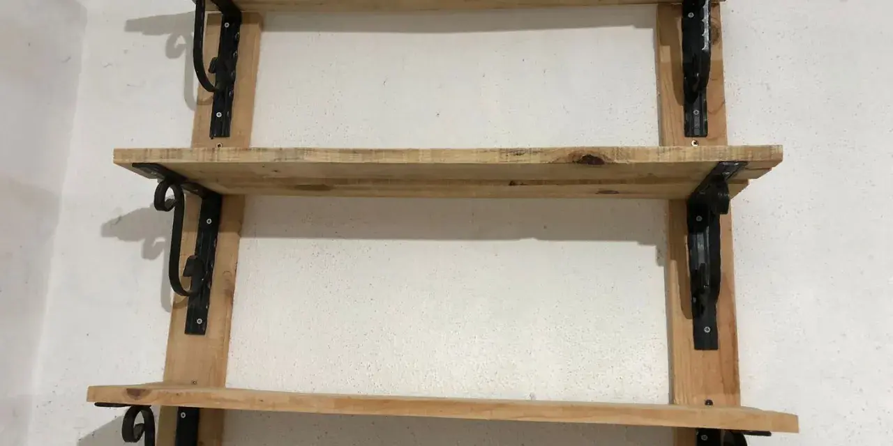 Scaffali fai da te garage: tre ripiani in legno grezzo, fissati a parete con staffe nere decorative. Perfetti per organizzare attrezzi e materiali.