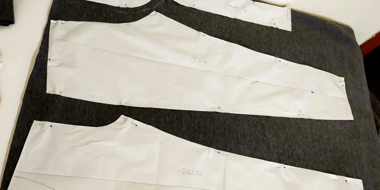 Wykroje papierowe do spodni (przód i tył) przypięte do ciemnego materiału. Rozpoczynamy proces, jak zrobić wykrój spodni.