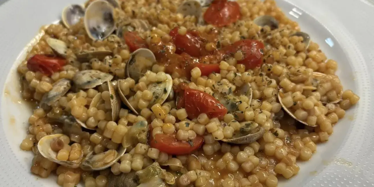 Un piatto invitante di fregola con vongole, pomodorini e prezzemolo, pronto per essere gustato.