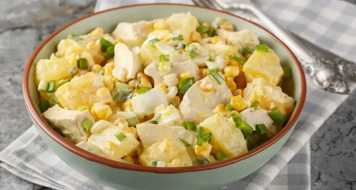 Una ciotola piena di insalata di pollo e patate, con mais, uova sode e cipollotto fresco.