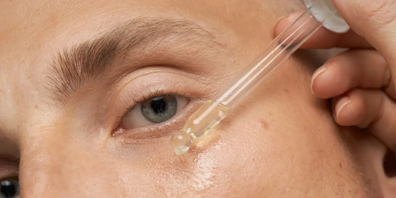 Nahaufnahme eines Auges, auf das ein Tropfen Öl aus einer Pipette aufgetragen wird.
