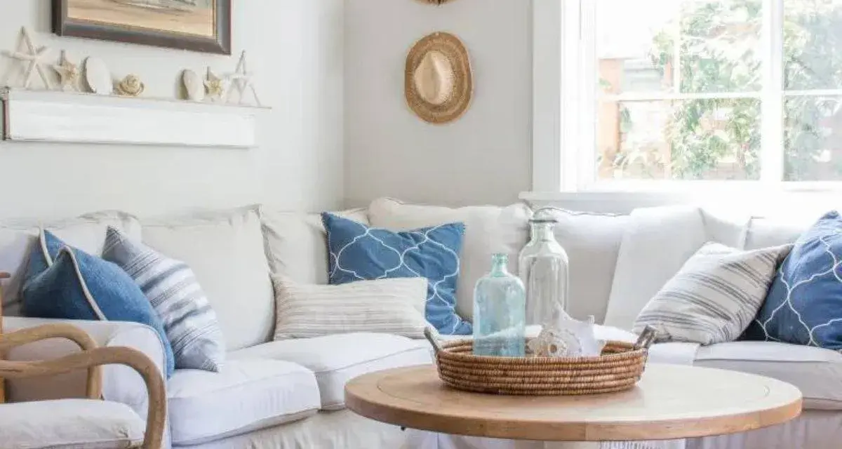 Un accogliente soggiorno con arredamento coastal: divano bianco, cuscini blu e bianchi, tavolino in legno e decorazioni marine.