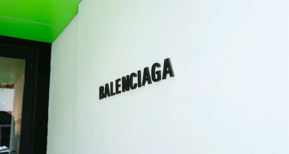 Il logo Balenciaga su una parete bianca, sotto un soffitto verde brillante. Chi è Balenciaga? Un nome che evoca alta moda e design audace.