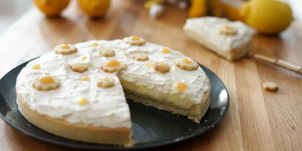 Tarte au citron décorée de petites fleurs en biscuit. Une part est coupée, révélant la crème pâtissière. Parfait pour une recette de tarte.