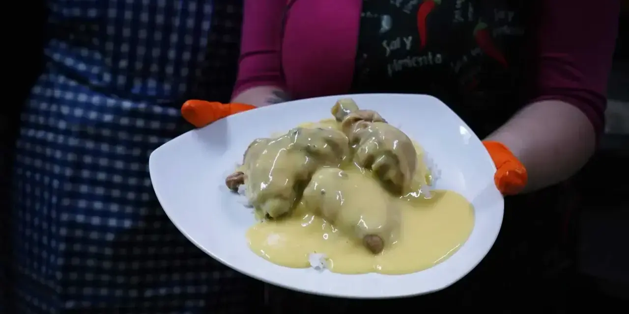 Porcja potrawki z kurczaka w kremowym sosie, podana na ryżu. Danie prezentowane na białym talerzu, trzymanym przez osobę w pomarańczowych rękawiczkach.