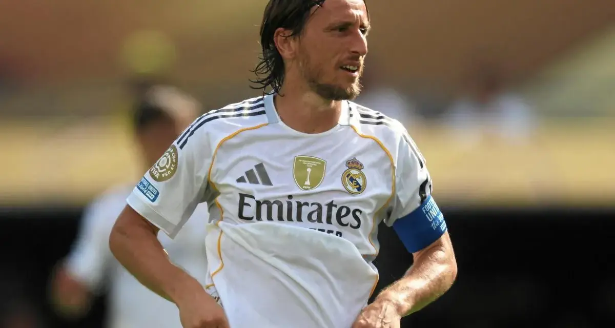 Luka Modrić w białej koszulce Realu Madryt, gdzie gra, z opaską na ramieniu.