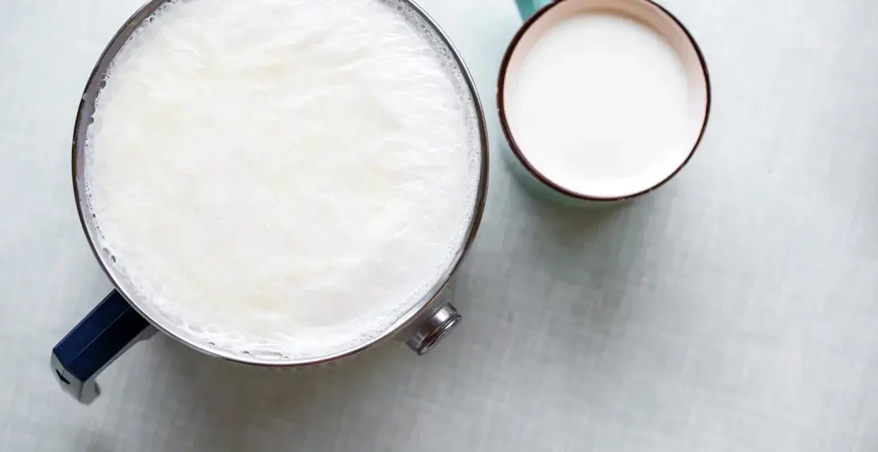 Un pot de lait chaud avec une fine peau de lait à la surface, à côté d'une tasse remplie de lait frais.