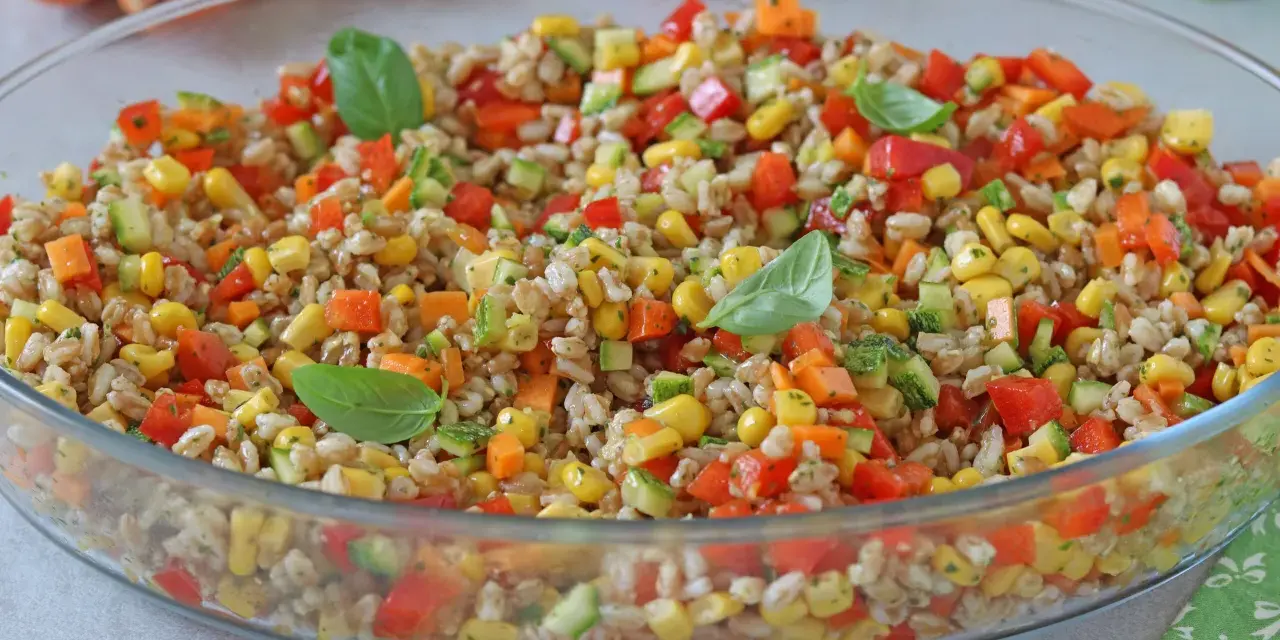 Insalata di farro colorata con mais, peperoni, zucchine e carote, guarnita con foglie di basilico fresco. Un piatto estivo e salutare.
